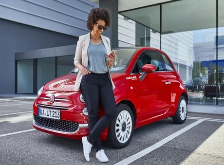 Frau lehnt am stadtmobil mit Handy in der Hand