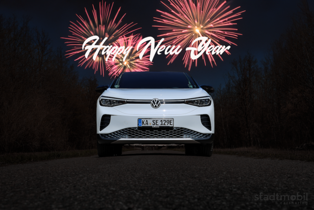 weißes stadtmobil, dahinter Feuerwerk und Neujahreswünsche