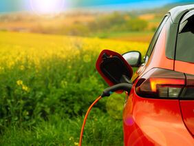 Ein Corsa-e steht an einer Ladesäule. Im Hintergrund blüht ein Rapsfeld.